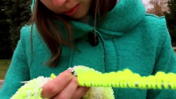 The girl in green gloves is knitting a sitting on the bench in the Park. — Stock Video