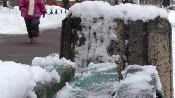 Antiguo banco verde en la nieve de cerca. En el fondo caminar piernas . — Vídeo de stock