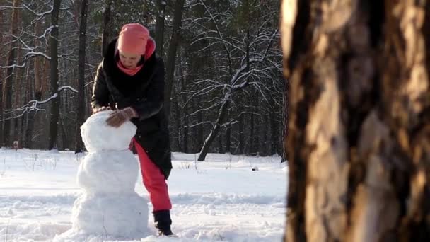 The girl makes snowman in winter in the woods. Frame of pines. — Stock Video