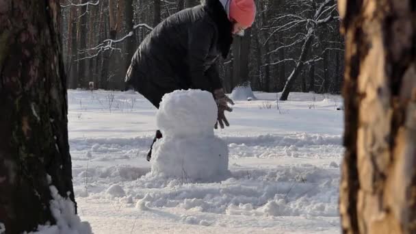 The girl makes snowman in winter in the woods. Frame of pines. — Stock Video