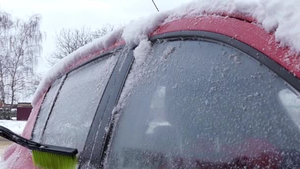 Das Mädchen räumt Schnee auf dem roten Auto. Action in Zeitlupe. rechte Seite. — Stockvideo