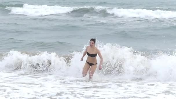 Молода дівчина в бікіні біжить на пляжі хвилями. Холодна вода. Повільний рух . — стокове відео