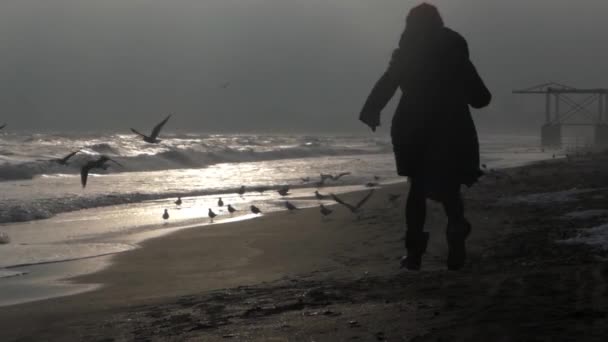 Silueta de una chica corre por la playa en ropa de invierno . — Vídeo de stock