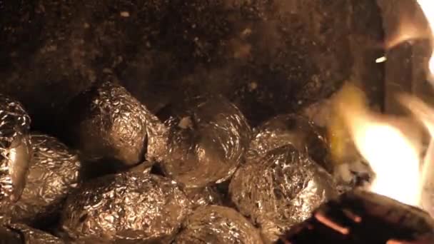 Pommes de terre enveloppées dans une feuille de cuisson dans les braises dans la cheminée . — Video
