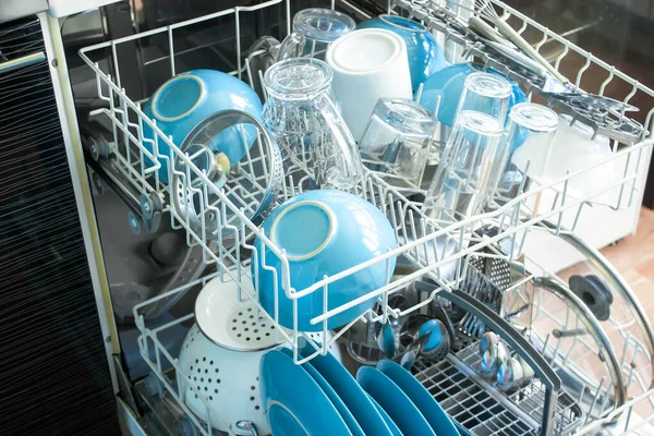 opened Dishwasher after cleaning process both baskets with clean dishes: bowls, glasses, close up
