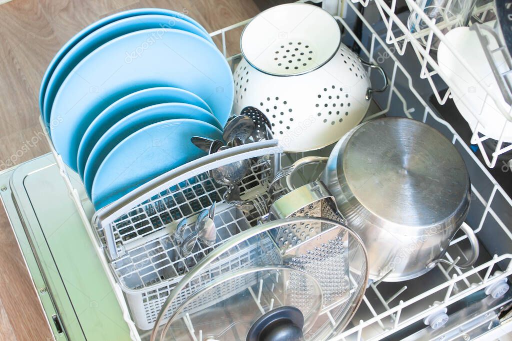 opened lower basket of Dishwasher after cleaning process with clean dishes: plates, pan, colander, close up