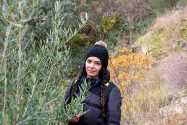 Ağaçların arasında kış şapkası olan beyaz, genç ve güzel bir kadının portresi. Meşe palamudu ve zeytin ağacı