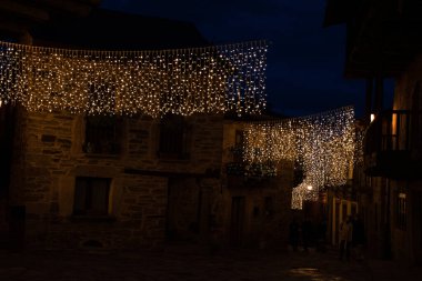 Noel 'de bir yıldız ve ışıkla aydınlatılmış bir caddenin yatay görüntüsü, taştan evler arasında yürüyen insanların arka planı.