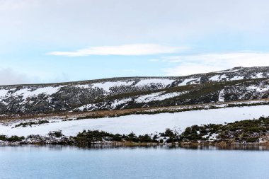 Sakin göl ve karlı dağ yatay görünüyor. Suyun kenarına kadar kar.
