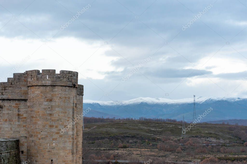 Horizontal panoramic view of a stone castle tower and snow-capped mountains in the background