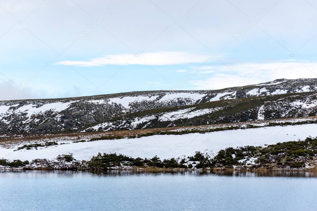 Horizontal view of the calm lake and a snowy mountain. Snow up to the water's edge