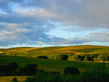 Parlak renklerle gün batımı. Yeşil bir çayırın yatay görüntüsü ve çok güçlü mavi bir gökyüzü. Dramatik bir görüntü. Rüzgar değirmenleri. Yenilenebilir enerji