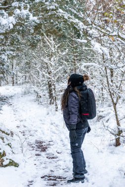 Genç kız karda atlamaya hazırlanıyor. Karlı ormanın dikey görüntüsü.