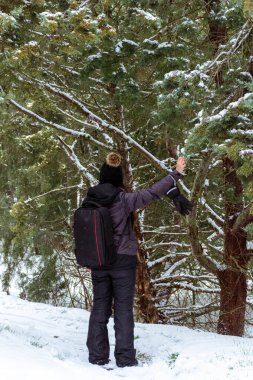 Sırtında beyaz beyaz bir kadının dikey görüntüsü ve sağ eliyle donmuş, karla kaplı bir ağacın dallarına dokunuyor. Kış kontrast. Kar ve buzla kaplı bir orman.