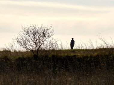 Kışın tepeye tırmanan bir adamın silüeti. Bulutlu bir gün. Yatay görünüm