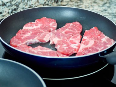 Tavada pirzola pişirmek. Çiğ et ızgara. Cam seramik hob 'da yemek pişirmek.