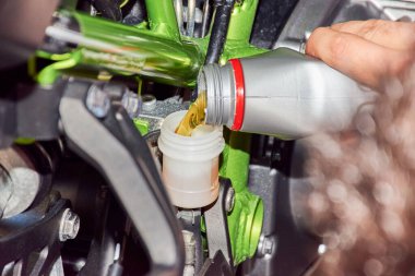 Tamirci bakım yapıyor. Bir motosikletin arka fren deposunu sıvıyla doldurmak. Sığ alan derinliğiyle seçici odaklanma. Bokeh ile arkaplan