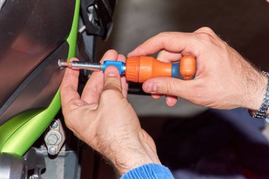 Motosiklet tamircisi vidaları söküyor. Geçmişi bulanık, yeşil ve siyah bir motosiklet. Genel mekanik için ergonomik araç