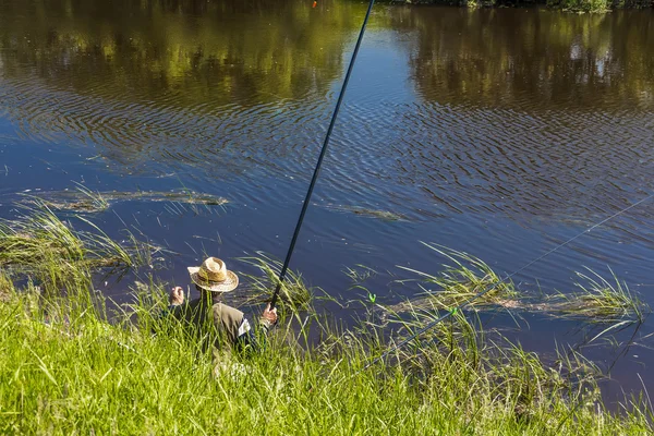 Рыбак в летний день рыбачит на реке на платформе — стоковое фото