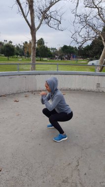 Parkta çömelme egzersizi yapan bir kadın.