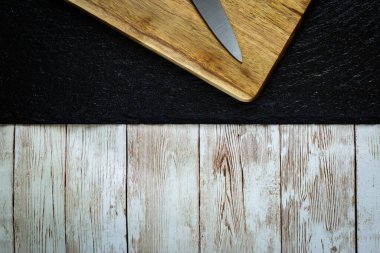 Küçük mutfak bıçağı ahşap kesme tahtasına yerleştirilmiş. Kabartmalı siyah taşın üstüne. Tahta masanın üstüne.