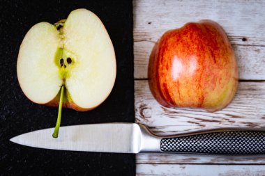 Tahtaya yerleştirilmiş yarım elma ve yanında bir bıçakla taş yüzeyler.