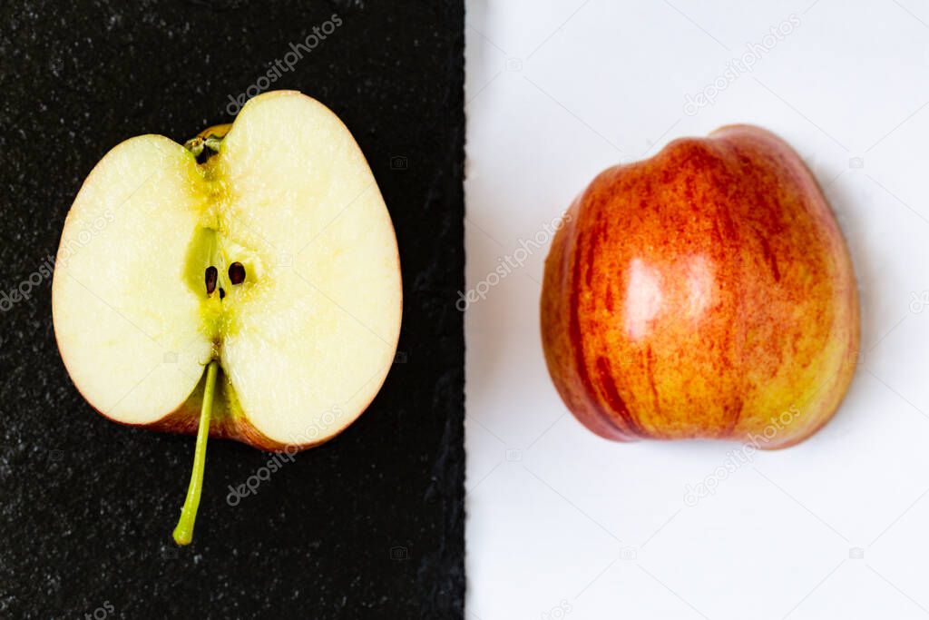 An apple sliced in half placed on contrasting black and white surfaces