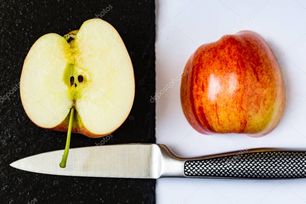 Two half of a sliced apple placed on white and black backgrounds next to kitchen knife