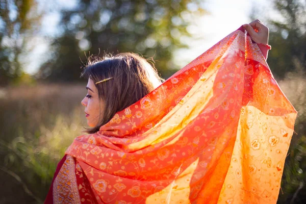 Woman\'s face in profile spreading traditional Indian fabric lit by the setting sun