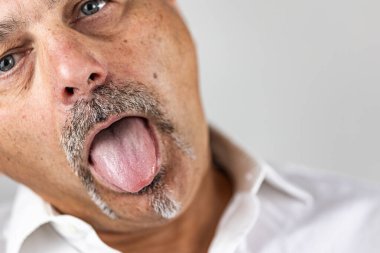 Yakın plan - sakallı ve bıyıklı yaşlı bir adamın beyaz arka planda izole edilmiş bir şekilde diline yapışması.