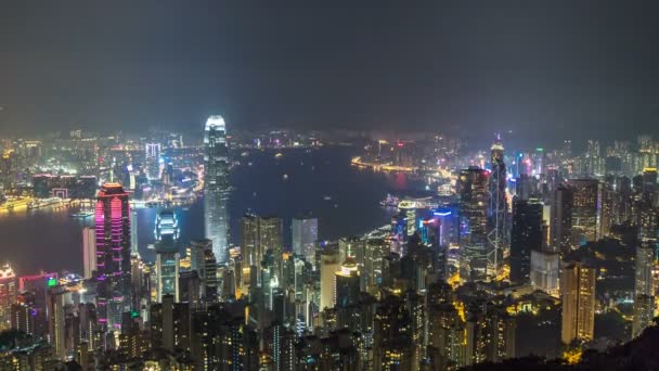 Hong Kong city skyline timelapse at night with Victoria Harbor and skyscrapers illuminated by lights over water viewed from mountain top. — Stock Video