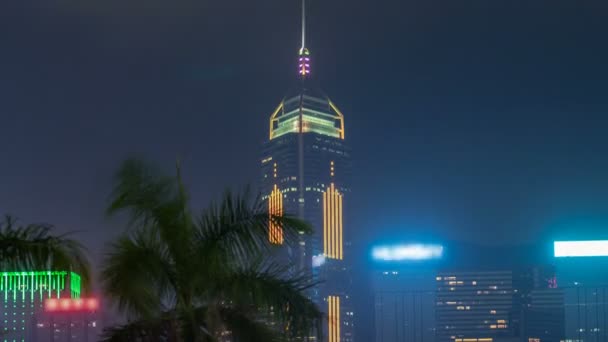 Vista da vicino del timelapse dei grattacieli futuristici e delle loro luci lampeggianti viste di notte con palma dal centro culturale di Kowloon — Video Stock