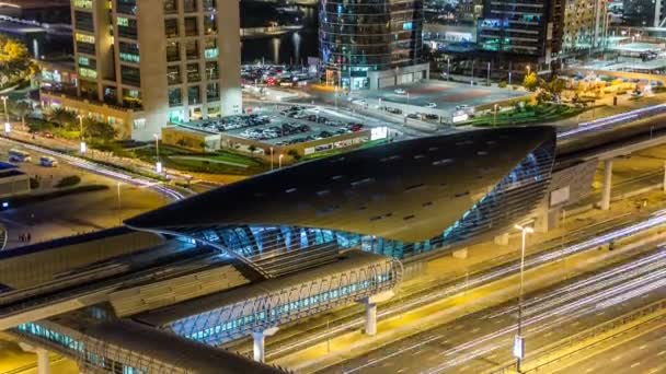Metro station near Buildings of Jumeirah Lakes Towers with traffic on the road night timelapse. — Stock Video