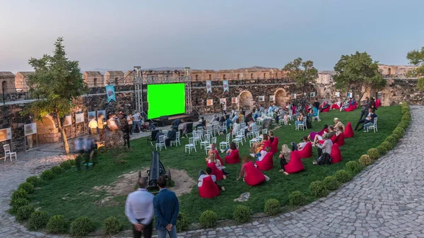 People are enjoying the open air cinema with green screen in the hictoric building at evening aerial timelapse after sunset. Chairs with social distancing during pandemic situation