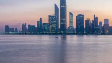 Abu Dabi şehri, gün doğmadan gökdelenlerle gökdelenlerle kaplandı. Gece gündüz su yansımasıyla birlikte.
