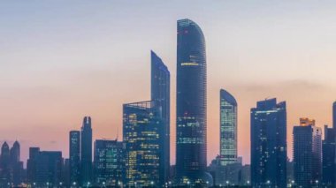 Abu Dabi şehri, gün doğmadan gökdelenlerle gökdelenlerle kaplandı. Gece gündüz su yansımasıyla birlikte.