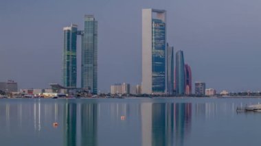 Abu Dabi şehri, gün doğmadan gökdelenlerle gökdelenlerle kaplandı. Gece gündüz su yansımasıyla birlikte.