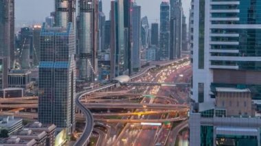 Dubai şehir mimarisi günden geceye kadar. Şeyh Zayed yolu üzerindeki aydınlık gökdelenleri ve trafik manzarası.