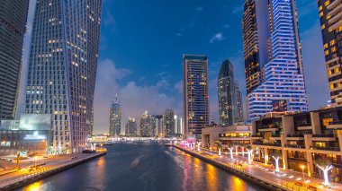 Dubai Marina rıhtımı. Köprüden gece, gündüz kuleleri ve yatları var. Geçiş zamanı, Birleşik Arap Emirlikleri. Gün batımından sonra gökdelenler ve kanallar