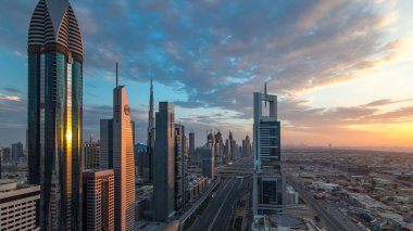 Dubai gökdelenleri akşam saatlerinde güneş camlarında yansıyor. Dubai metro istasyonu ve Şeyh Zayed Yolu 'ndaki trafik. Kule çatısından gökyüzü görüntüsü. Renkli bulutlu gökyüzü ve güneş ışığı