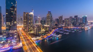 Dubai, BAE 'de gün batımından sonra yüzen yat ve teknelerle Dubai Marina gezinti güvertesi ve kanalı üzerinden geçen güzel bir gökyüzü çizgisi. Modern kuleler ve köprüdeki trafik.
