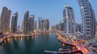 Hava üst görüntüsü, günden geceye geçiş zamanı. Dubai Marina gezinti güvertesi ve kanalı, gün batımından sonra Dubai, BAE 'de yüzen yatlar ve teknelerle dolu. Modern kuleler ve trafik