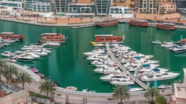 Dubai Marina körfezindeki iskeleye park etmiş lüks yatlar. Şehir hava manzaralı zaman ayarlı. Sabah erken saatlerde kuleler ve gökdelenler