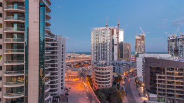Dubai Marina 'da aydınlık gökdelenler ve gece gündüz gezinti güvertesi geçiş zamanı. Yol trafiği olan modern kuleler ve tekneler. Birleşik Arap Emirlikleri
