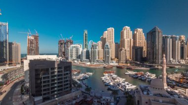Dubai Marina 'daki yatlar El Rahim Camii tarafından kuşatılmış ve tüm gün boyunca gölgeler hızla ilerlerken gökdelenler ve kuleler havalanmıştır. Tekneler ve ahşap çayırlarla modern gökdelenler.