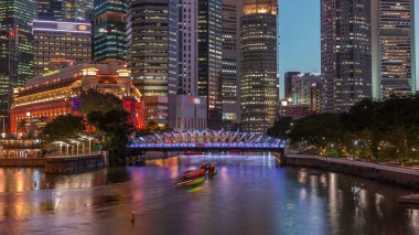 Singapur gökdelenleri beyaz Anderson Köprüsü ve Escplanade Park yakınlarındaki birkaç finans bölgesi kulesi ile gökdelenden geceye geçiş zamanı. Her iki tarafta da yeşil yapraklar var..