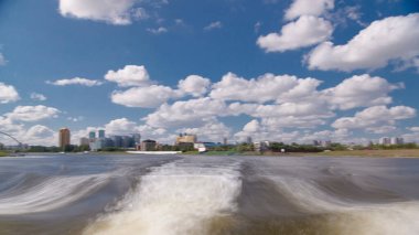 Astana, Kazakistan. Keyif teknesinden Astana 'da Ishim nehrinde hareketli bir seyahat görüntüsü. Mavi gökyüzü ve bulutlarla dolu bir yaz gününde. Bulanık hareket