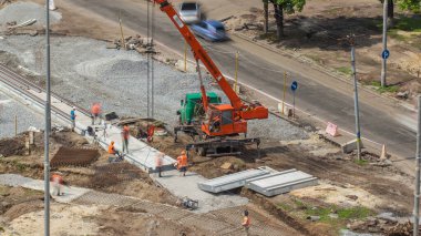 Yol inşaatı zamanına vinçle beton plakalar yerleştiriliyor. Şapkalı ve üniformalı endüstriyel işçiler. Havadan görünüşlü. Şehir Bulvarı 'ndaki tramvay raylarının yeniden inşası