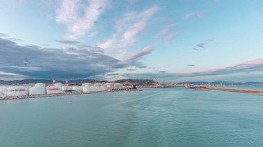 Gün batımında açık denizde yelken açan gemiden dalgalı ve limanlı deniz manzarası. Barselona kıyısı, İspanya