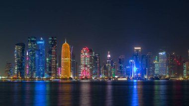 Doha şehir merkezi ufuk çizgisi günden geceye geçiş zamanı, Katar, Orta Doğu. Batı Körfezi 'ndeki aydınlık gökdelenler Körfez suyuna yansıyor.